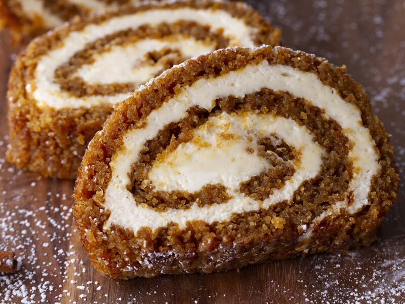Two slices of pumpkin roll cake on a wooden board, dusted with powdered sweetener.