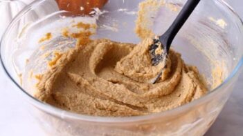 A mixing spoon inside pumpkin cake batter in a bowl.