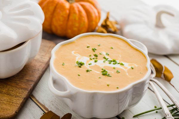 thick, creamy pumpkin soup in a white bowl with cream on top