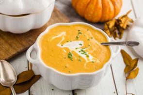 a spoon in a bowl of orange pumpkin soup with cream on top and chives