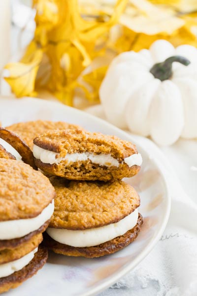 a bite out of a pumpkin whoopie pie stacked on a whole one with a white pumpkin in the background