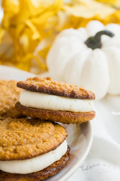 two pumpkin cookies filled with a cream cheese filling in front of a white pumpkin
