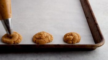 piping pumpkin cookies on a parchment lined baking sheet