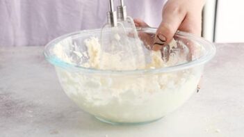 mixing a cream cheese frosting with an electric mixer while holding the bowl
