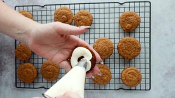 piping cream cheese filling to one side of a pumpkin cookie