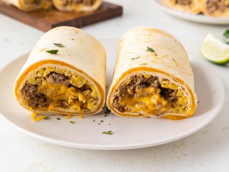 Two melty burritos on a plate filled with beef and cheese.