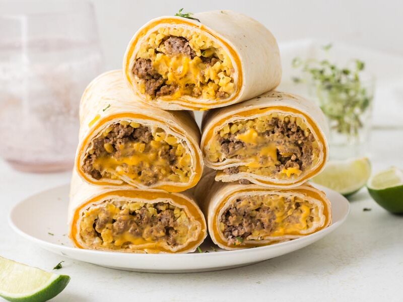 A stack of quesarito burritos on a plate cut in half to show the beef and cheese filling.
