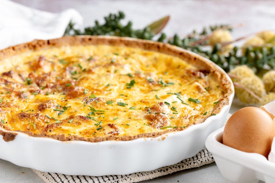a quiche in a white tart pan with an egg in front