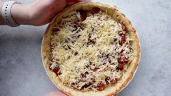 holding a tart pan filled with cooked bacon and cheese inside a pastry crust