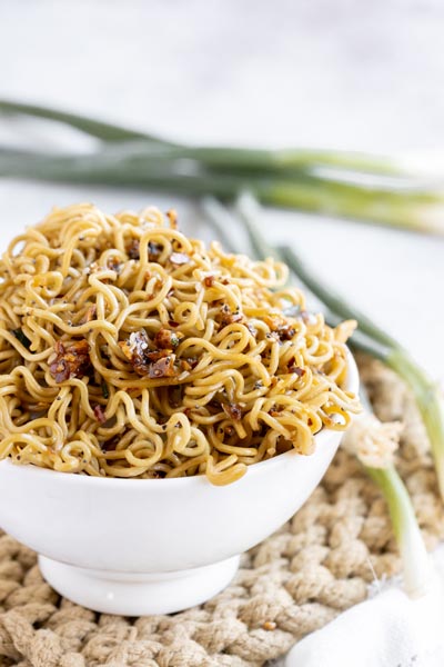 a bowl of ramen noodles sits in front of green onions