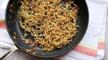 ramen noodles in a skillet covered in a sauce with red pepper flakes
