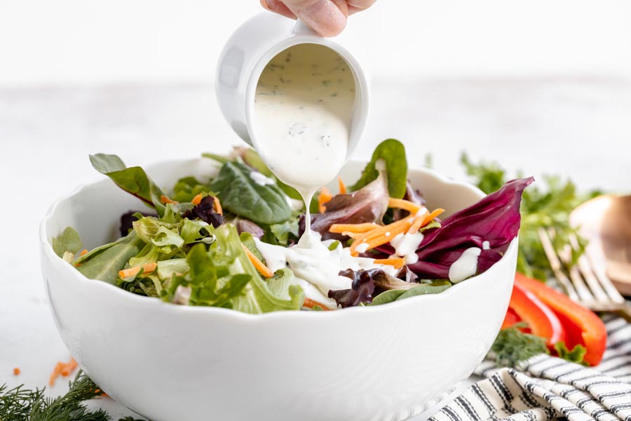 pouring creamy ranch dressing a a salad of green lettuce, matchstick carrots and bell pepper