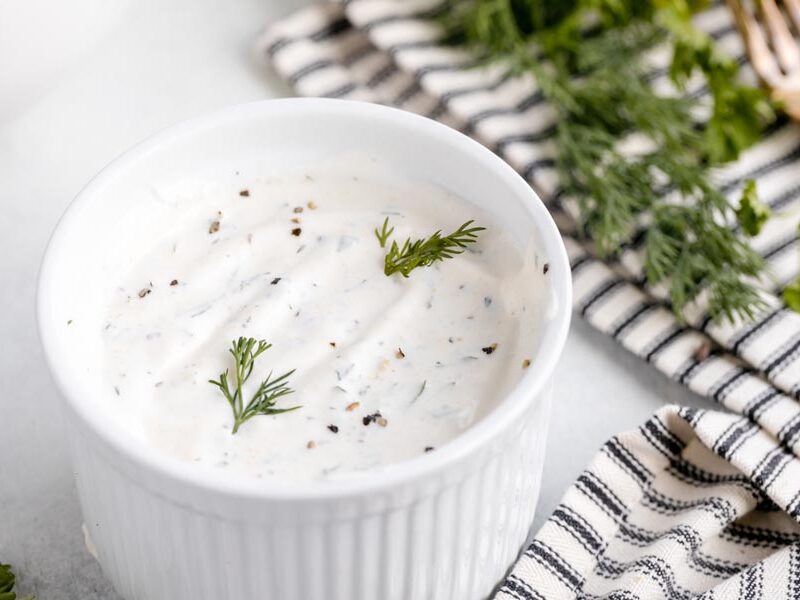 a ramekin with a creamy ranch dressing dip inside topped with cracked pepper and fresh dill