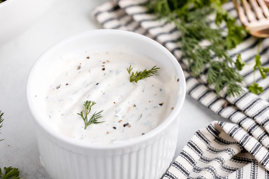 a ramekin with a creamy ranch dressing dip inside topped with cracked pepper and fresh dill