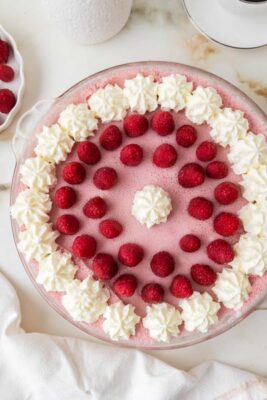 An overhead view of a whole keto raspberry marshmallow cream pie decorated with whipped cream and fresh raspberries.