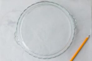 Glass pie dish lined with parchment paper for raspberry marshmallow cream pie.