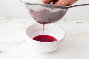 Fresh raspberry puree being strained through a fine-mesh sieve to remove the seeds.