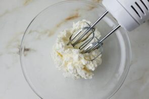 Cream cheese being whipped with an electric hand mixer until smooth and creamy.
