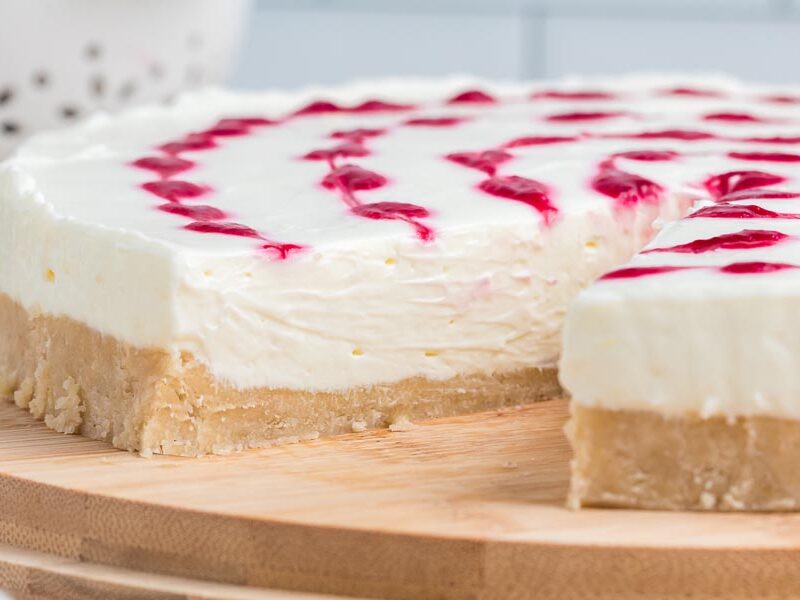 A slice of cheesecake taken out of the whole cheesecake on a wooden board.