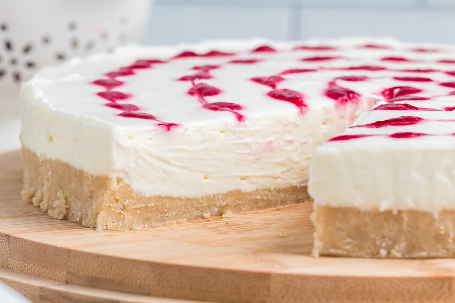 A slice of cheesecake taken out of the whole cheesecake on a wooden board.