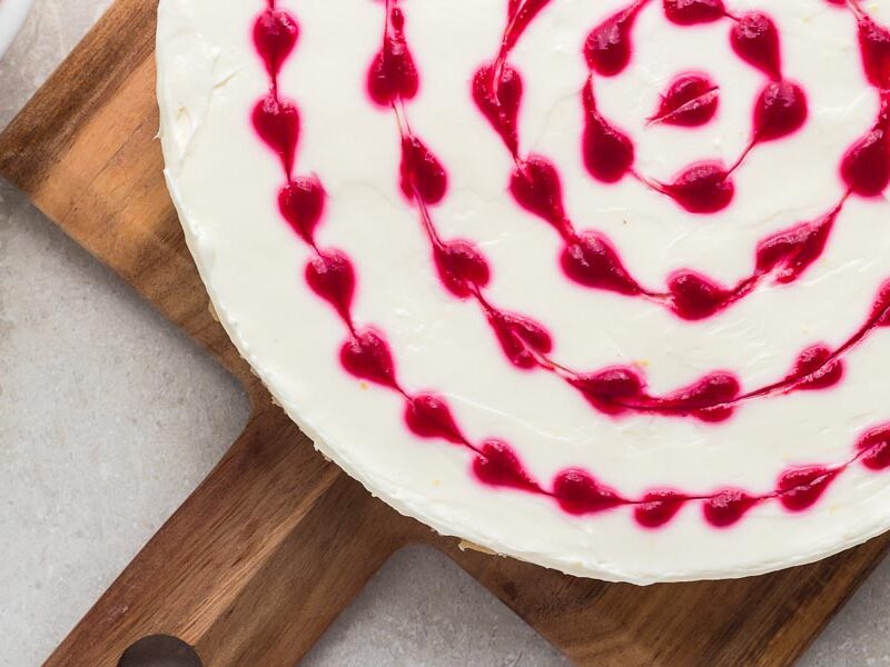 Red heart swirls of raspberry syrup are on top of a white cheesecake.