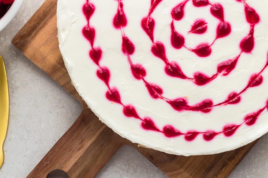 Red heart swirls of raspberry syrup are on top of a white cheesecake.
