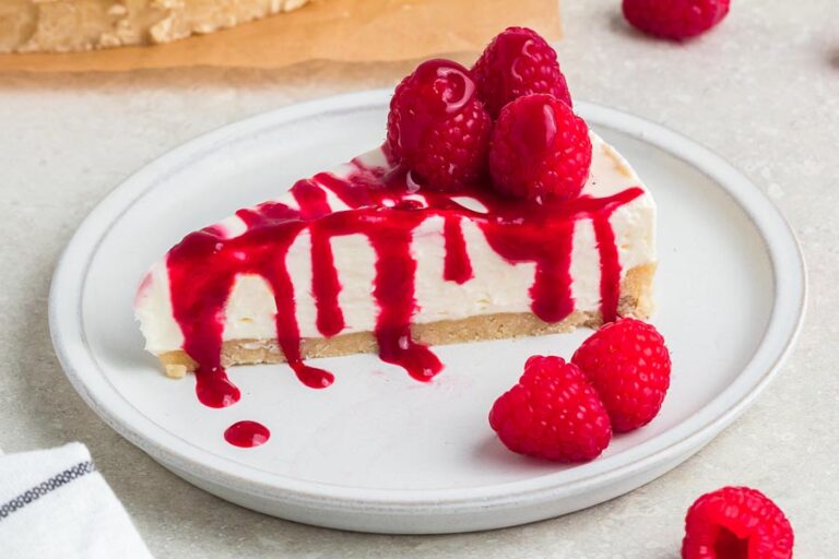 A slice of no-bake cheesecake on a plate covered with raspberry sauce and whole fresh raspberries.