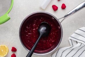 A spoon resting in a saucepan with raspberry puree.