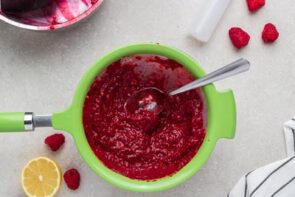 A spoon resting in strainer filled with raspberry puree.