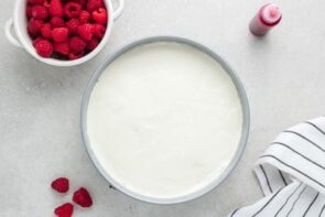 A plain no-bake cheesecake next to a bowl of fresh raspberries.