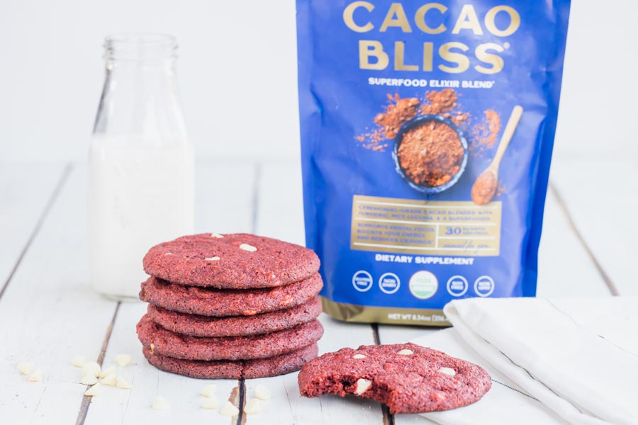 a stack of red cookies with cacao bliss and milk behind
