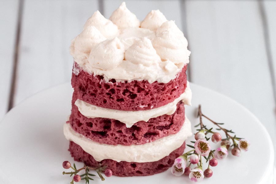 frosted keto red velvet mug cake on a white cake stand with flowers