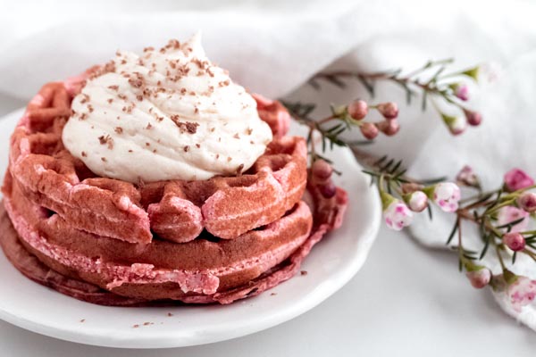stack of keto red velvet waffles topped with cream cheese frosting on the breakfast table