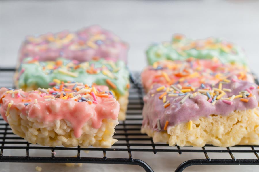 frosted rice crispy treats sitting on a wire rack while chocolate melts