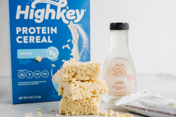 a box of highkey protein cereal with a stack of rice crispy treats and white chocolate