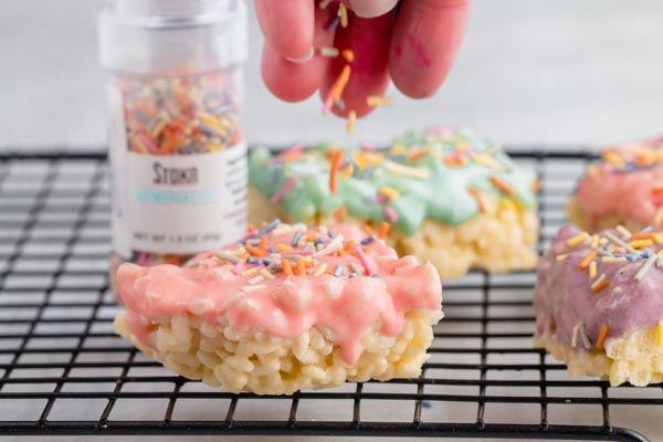 sprinkling colorful sugar-free sprinkles on top of a pink frosted rice crispy treat