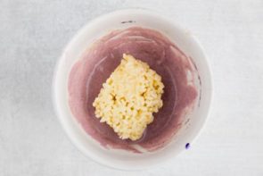 dipping a sugar-free rice crispy treat into a bowl of purple melted white chocolate