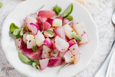cooked diced radishes on a plate with fresh herbs sprinkled on top