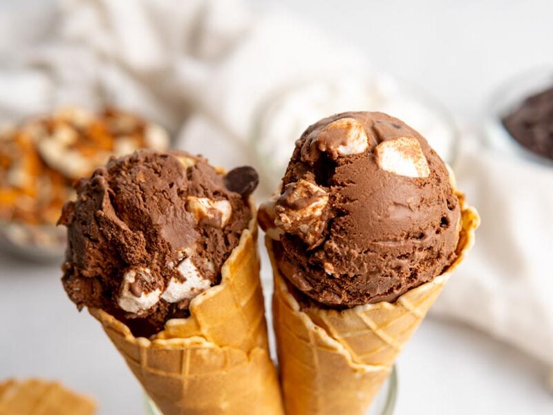 Two ice cream cones filled with a scoop of rocky road ice cream sit side by side.