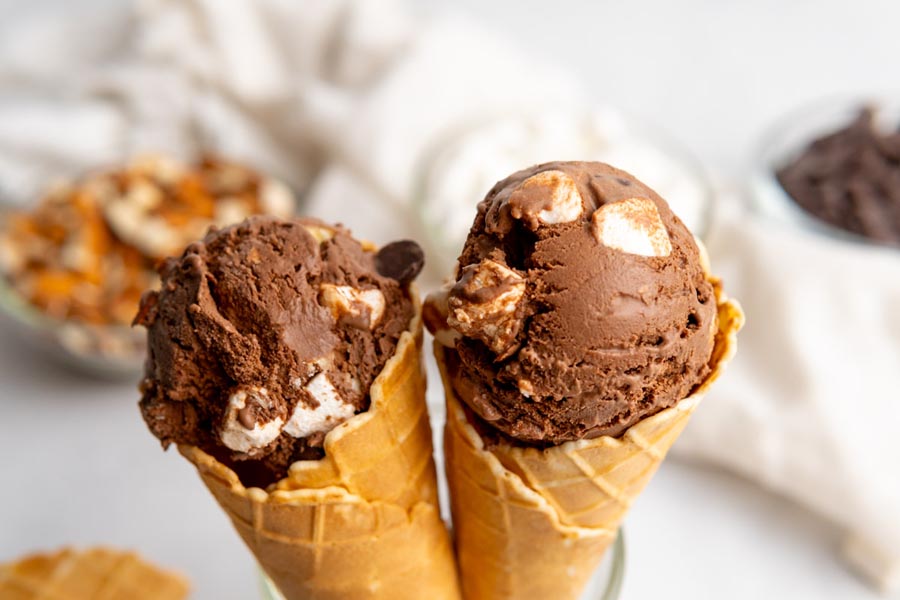 Two ice cream cones filled with a scoop of rocky road ice cream sit side by side.