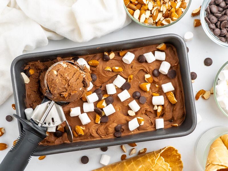A tub of rocky road ice cream covered with mini marshmallows, almonds and chocolate chips.