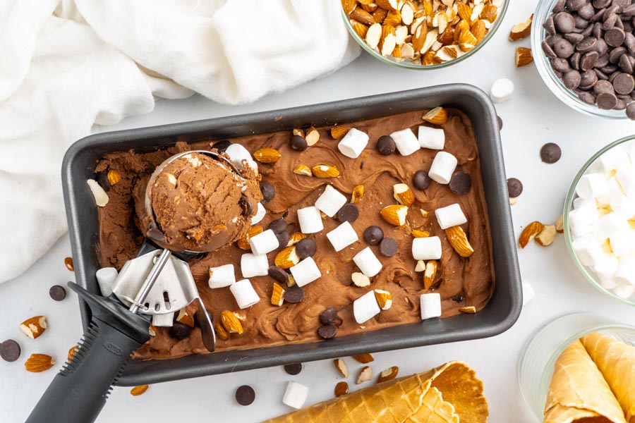 A tub of rocky road ice cream covered with mini marshmallows, almonds and chocolate chips.