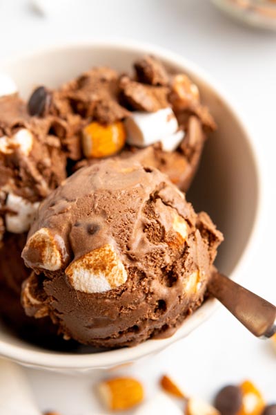 A bowl of creamy sugar free rocky road ice cream with chunks of marshmallows, nuts and chocolate in the chocolate ice cream.