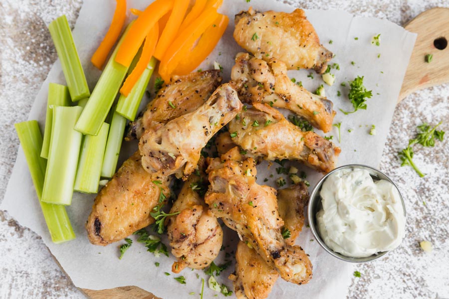 crispy wings on parchment paper served with celery sticks and julienned bell pepper
