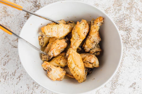 grabbing wings with tongs to coat with vinegar mixture