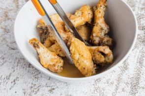 holding a chicken wing with tongs while tossing in marinade