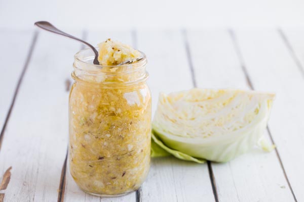 a folk holding a bunch of sauerkraut next to a wedge of cabbage