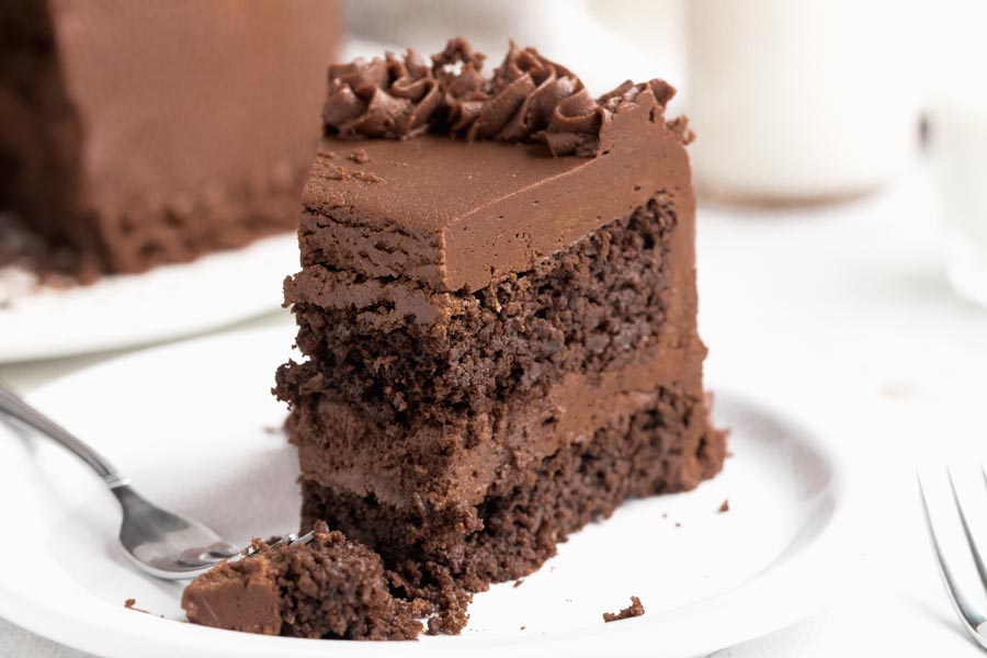 A bite taken out of a slice of chocolate cake on a plate.