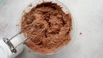 An electric mixer sits over a bowl with chocolate cake batter inside.