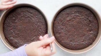 Hands sliding a butter knife around the edges of a baked chocolate cake to loosen the edges.